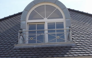 Absturzsicherung bestehend aus Edelstahlrahmen aus Flacheisen mit diagonalen Verstrebungen und Messingring mit aufgesetztem Handlauf.