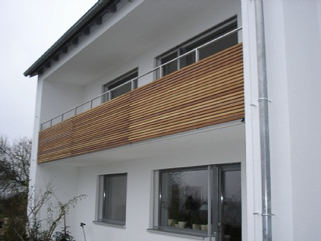 Balkongeländer bestehend aus Rechteckrohr-Rahmenkonstruktion, Material 1.4301 K240, 40x20x2mm, Verkleidung aus Lärchenholz, stirnseitig an Betonkante befestigt.