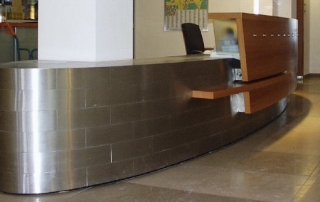 Empfangstheke aus Edelstahlverkleidung 1.4301, K240 geschliffen, mit Holzerhöhung für Ablage.